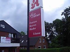 Salon O'Hara-Schild, rot und weiß, mit den Dienstleistungen: Damen, Herren, Kinder, Friseur, neben einem Gebäude.