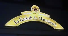Goldenes gewölbtes Schild: „La Kasbah de Marrakesch“ mit einem Kamelsymbol auf dunklem Hintergrund.