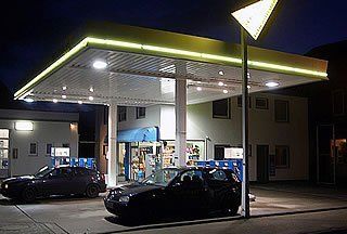 Tankstelle bei Nacht mit Autos unter dem Vordach, beleuchtet von Lichtern.