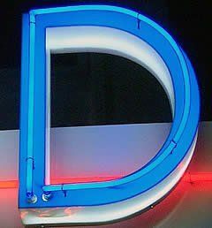 Blauer Neonbuchstabe „D“ auf weißem und schwarzem Hintergrund, mit rotem Licht unten.