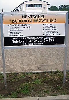 Schild für Hentschel, eine Tischlerei und ein Bestattungsunternehmen, mit einem Gebäude im Hintergrund.