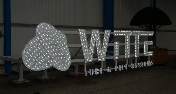 Schild für „Witte Tech & Fire Systems“ mit hellen weißen Lichtern auf einer weißen Metallstruktur.