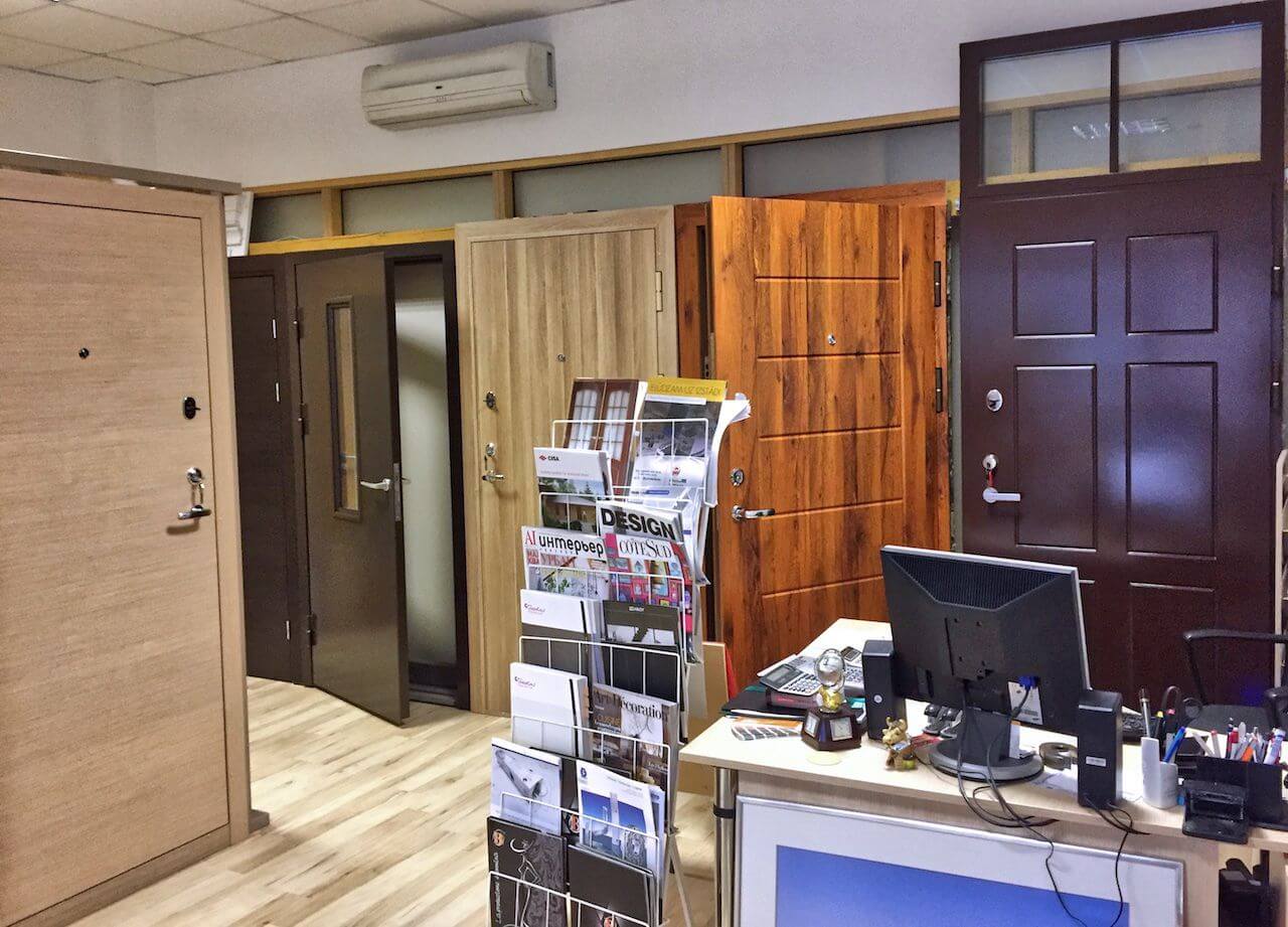 Interior of a door showroom with various door styles on display; a desk with computer and brochures.