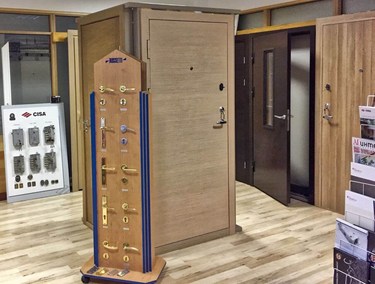 A door showroom with various doors, lock displays, and brochures on a wood floor.