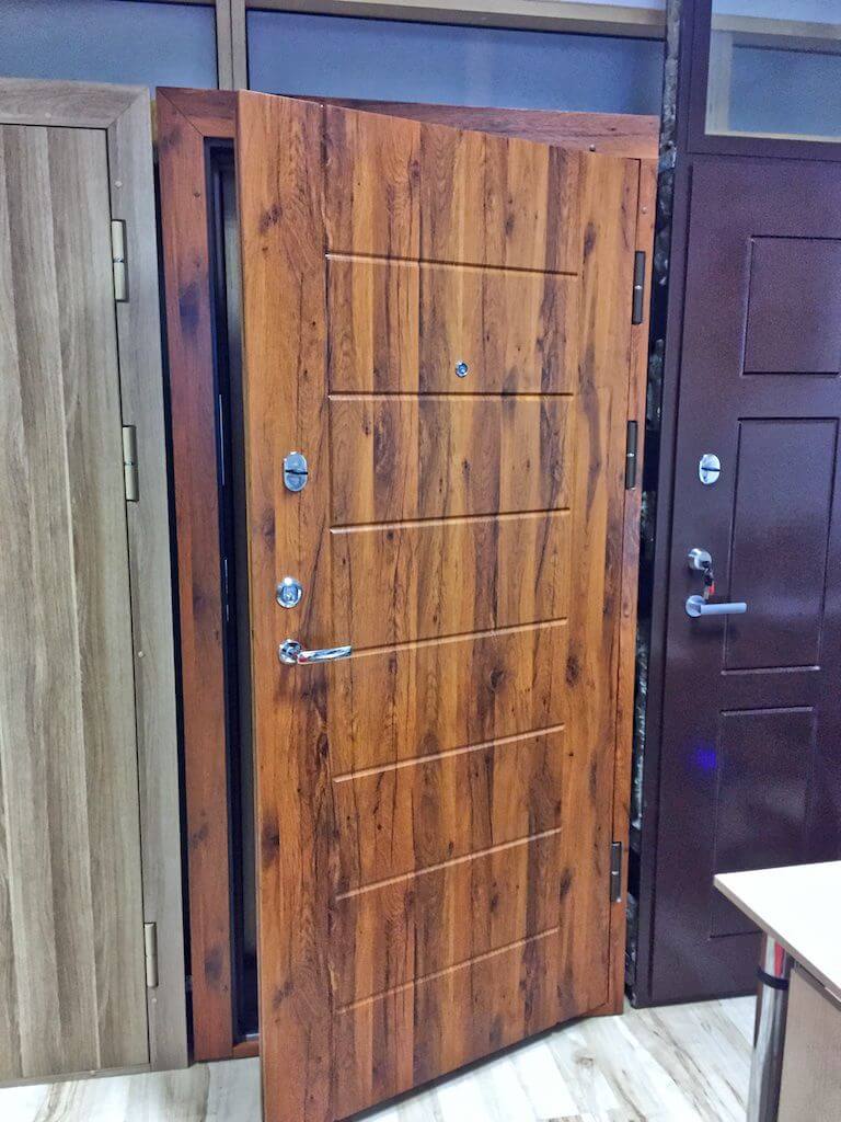 Wooden-textured metal door slightly ajar, showcasing its design. Other doors are visible on either side.
