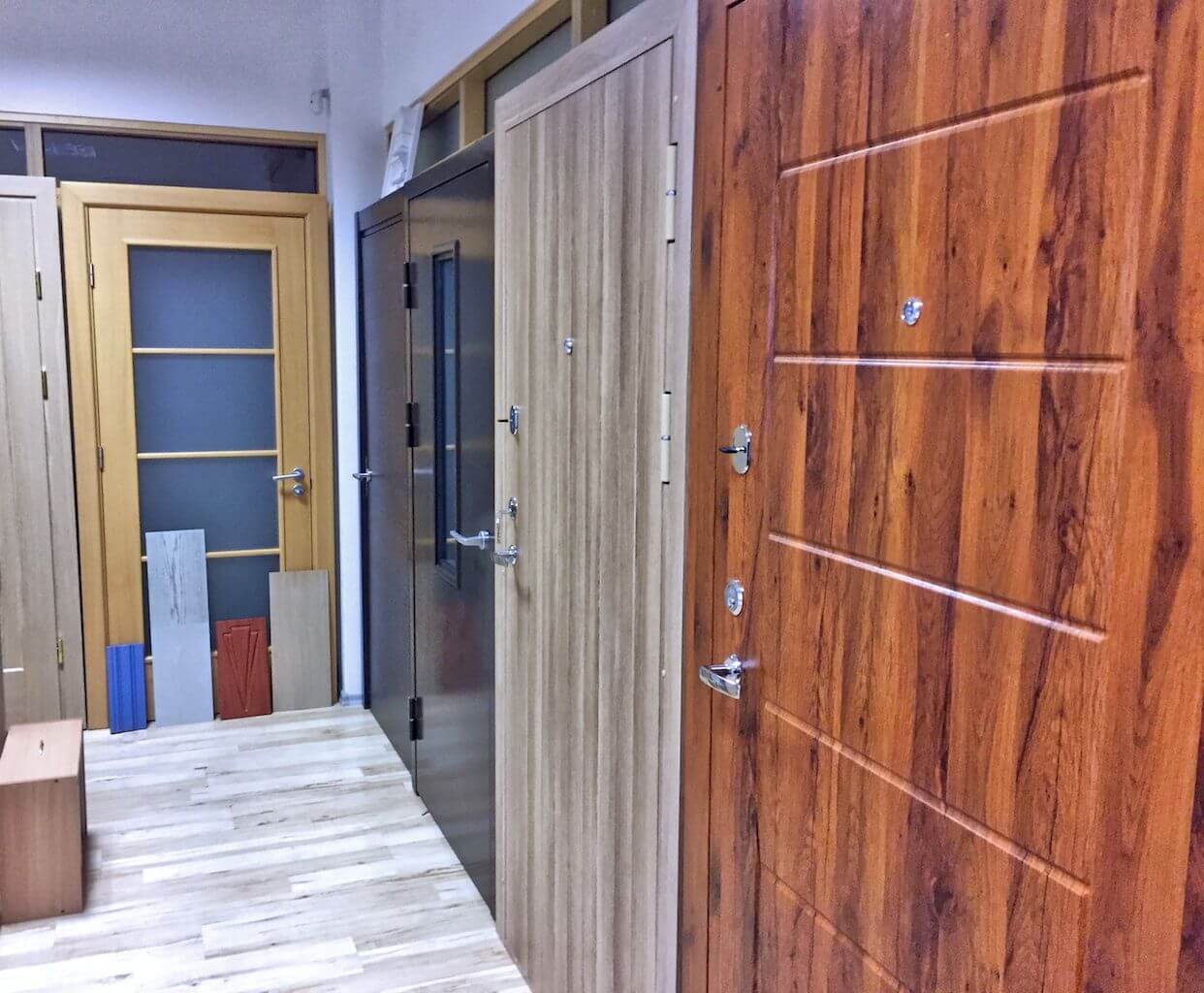 Interior door display in a showroom, various wood grain and solid color finishes, multiple door styles, hardwood flooring.