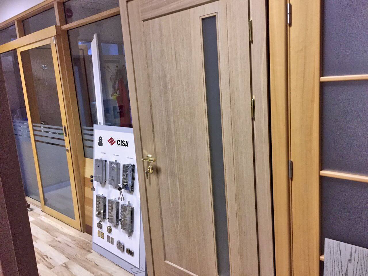 Wooden interior door with glass panel and hardware display in a showroom.
