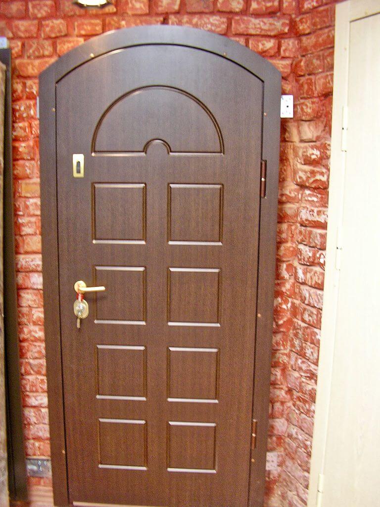 Brown wooden door with arched top, key in the lock, set in a brick wall.