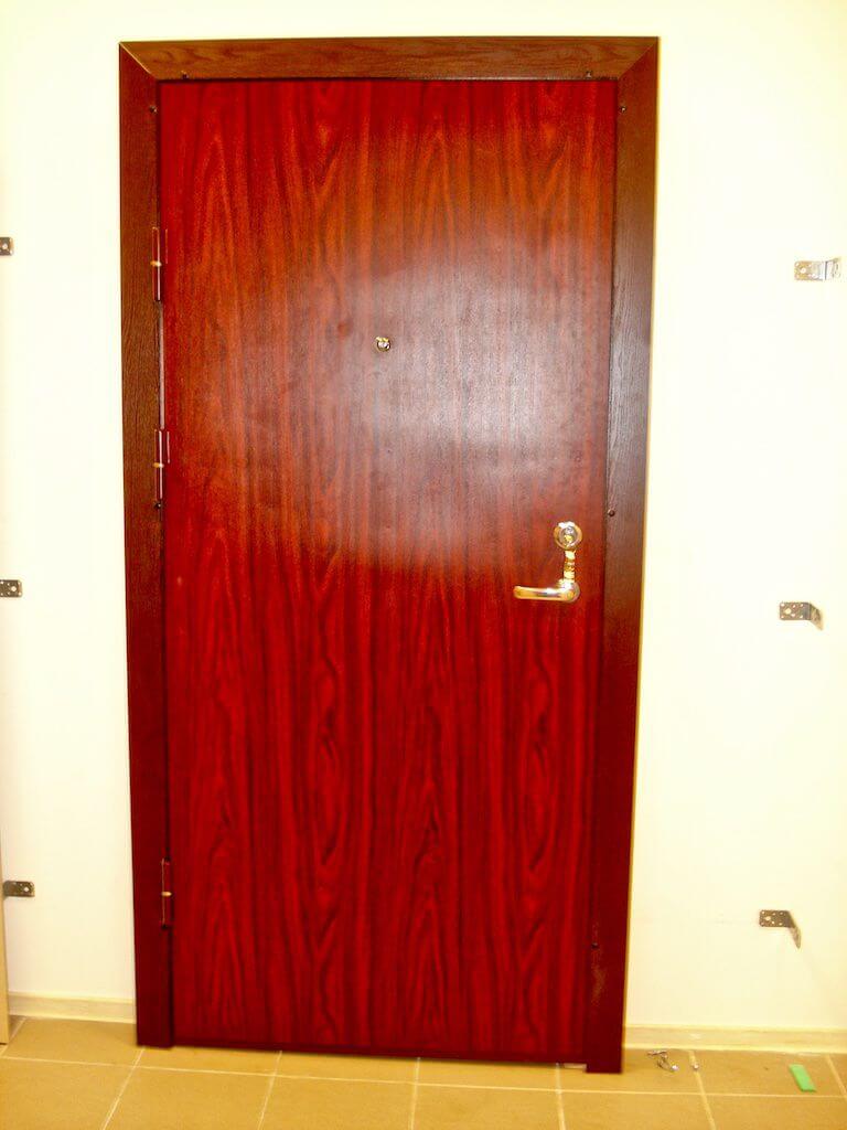 Wooden door with dark wood grain, set in a matching frame. The door has a handle and peephole.