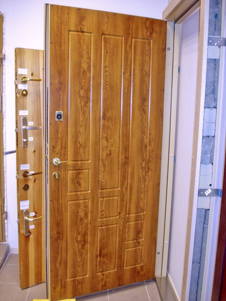 Brown textured wooden front door, rectangular panels, gold hardware.