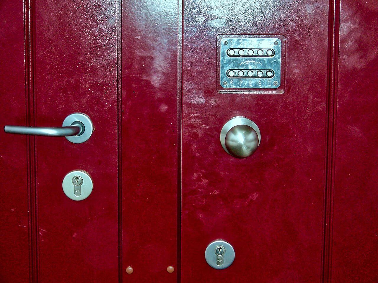 Red double door with combination lock, handle, and two keyholes.
