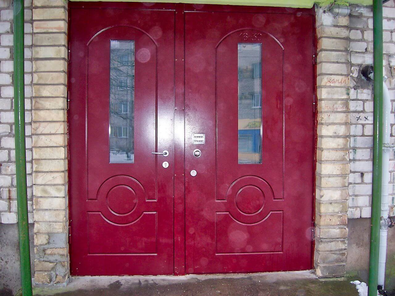 Red double doors with glass panels and a circular design, set in a brick doorway.