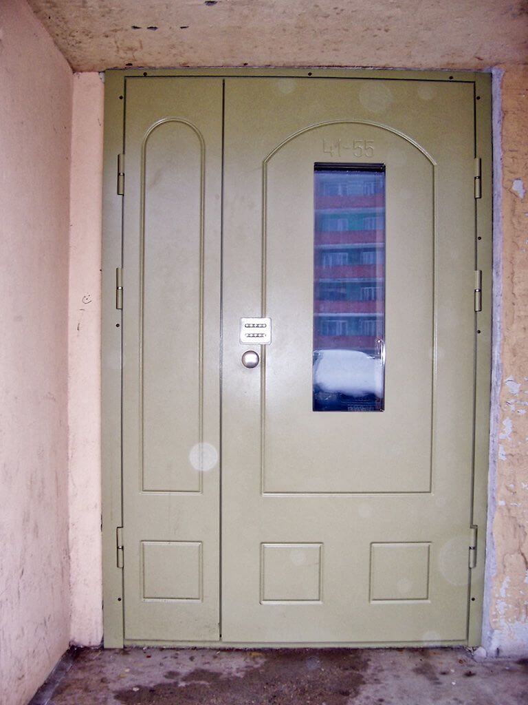 Tan metal building door with small window, small door handle, and white label.