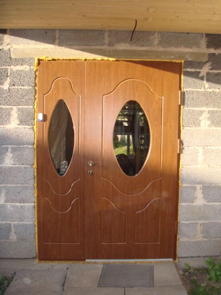 Brown double door with oval glass panes, set in a gray cinder block wall.