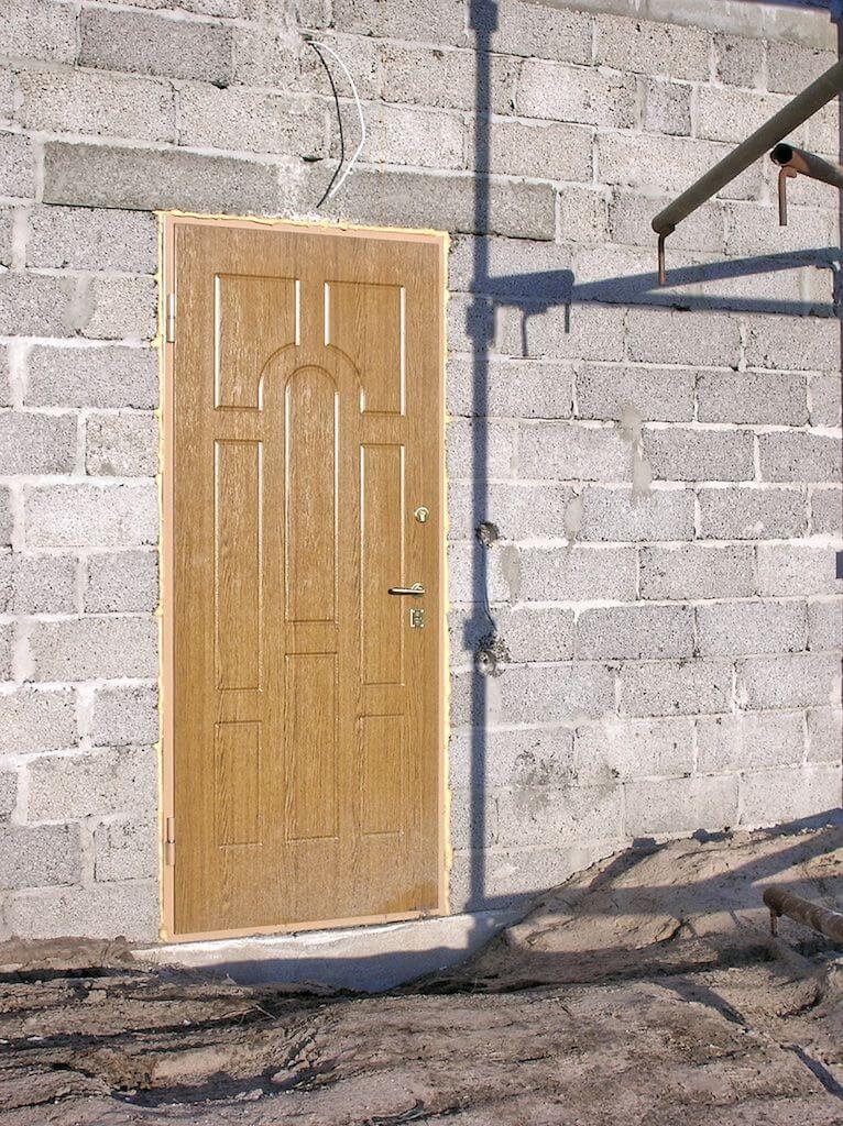 Tan door set in a gray cinder block wall, with a shadow cast across the wall.