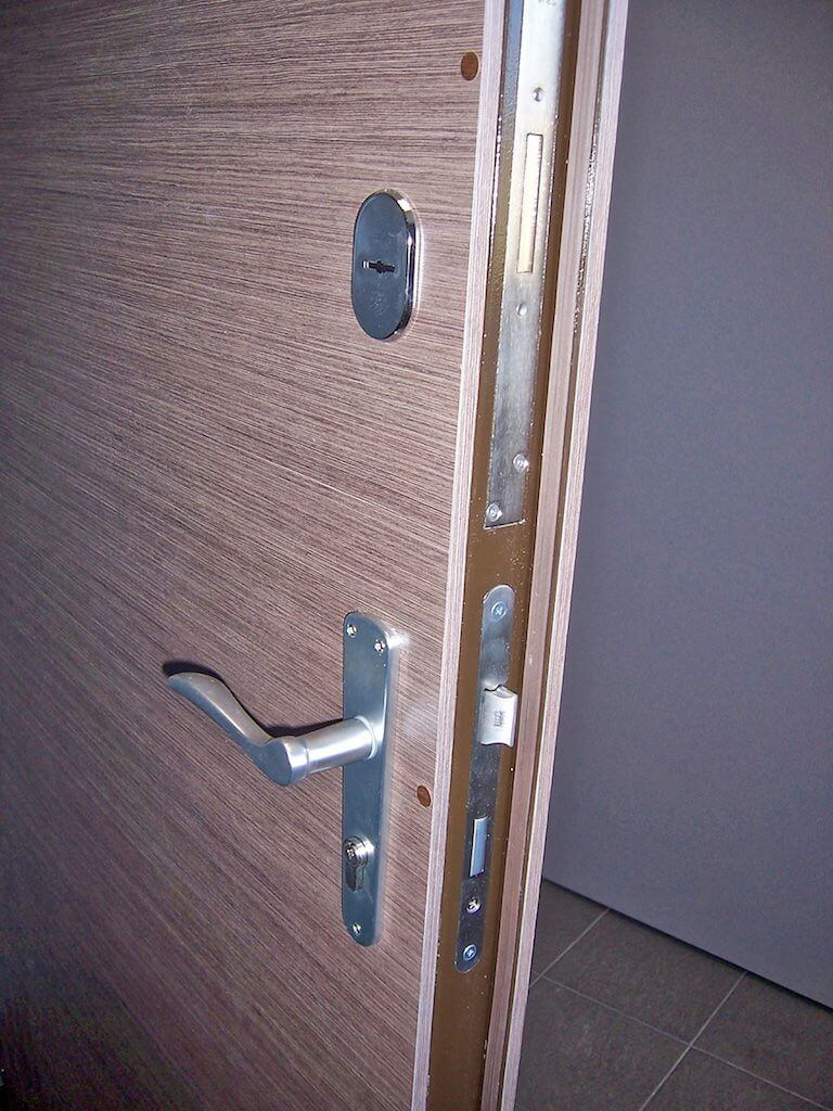 A closed wooden door with a silver handle, lock, and security features.