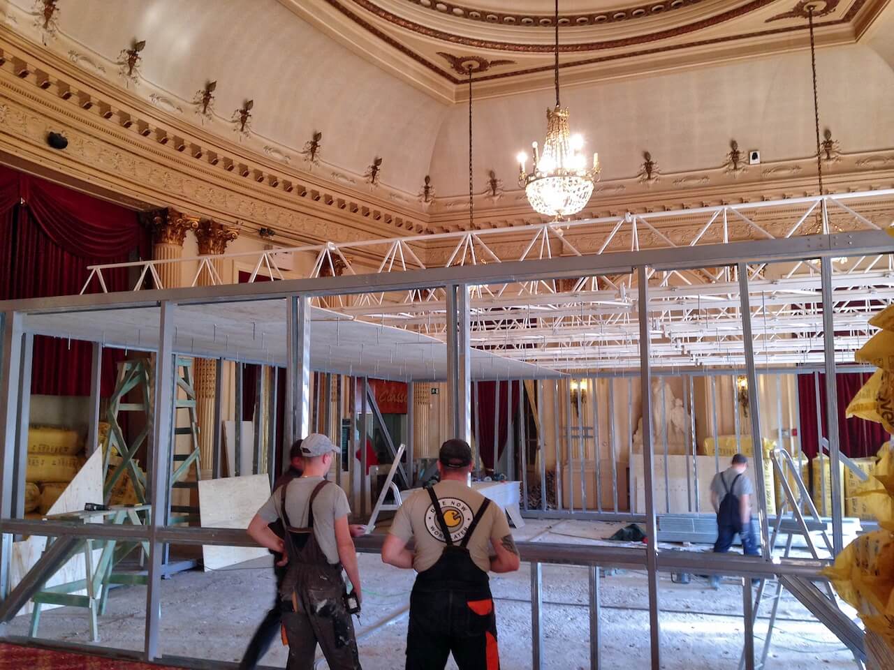 Two men standing in a large room with a chandelier hanging from the ceiling