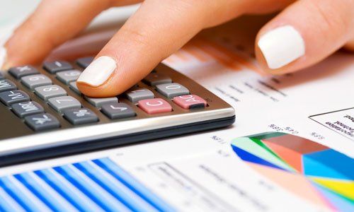 Hand using a calculator beside financial charts and graphs on a desk