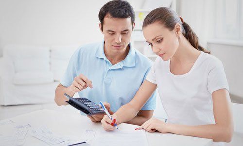 Two people reviewing documents at a table, one using a calculator and the other writing notes.