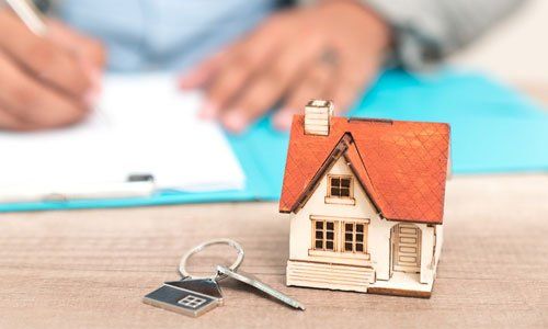 Toy house key with keychain on desk, with hands signing papers in the background