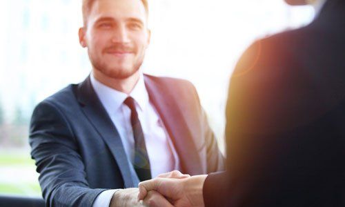 Businessman in a suit shaking hands across a bright office setting
