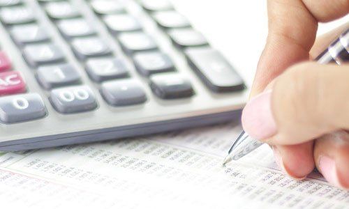 Hand counting numbers on a calculator beside a financial spreadsheet with a pen