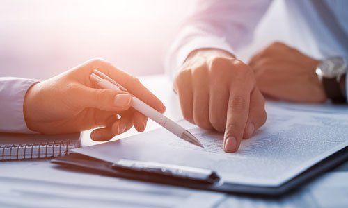 Two hands pointing at a document beside a notebook and pen on a desk