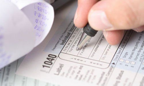 Hand filling out a tax form with a pen on a desk