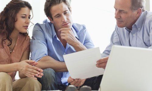 Three people in a meeting reviewing documents beside a laptop