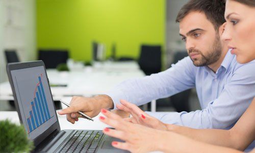 Two colleagues reviewing a laptop chart in a bright office, one pointing at the screen.