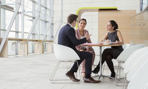 Three people talking at a modern office table in a bright, open workspace