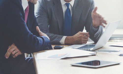 Business meeting at a desk with two people, laptop, papers, and a smartphone in a bright office.