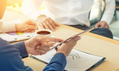 Hands reviewing charts and a tablet at a meeting table with coffee cups