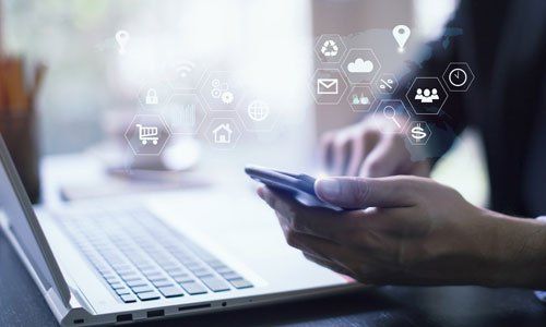 Hands using a smartphone beside a laptop with floating digital app icons