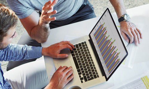 Hands around a laptop showing colorful charts and graphs on a white table