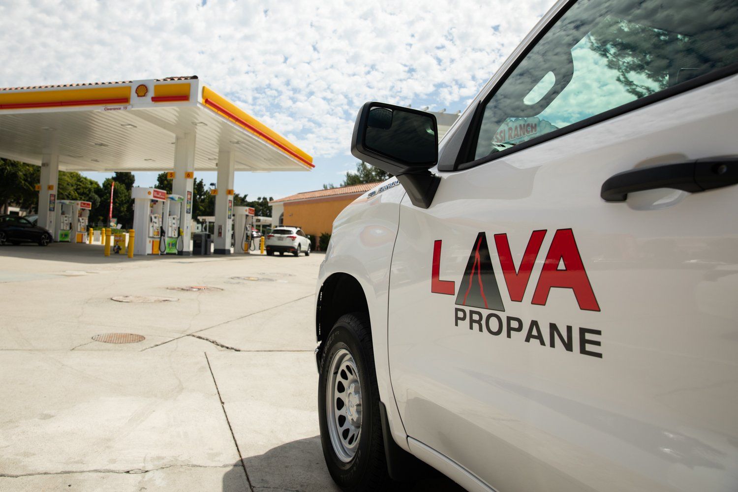A white lava propane truck is parked in front of a gas station.