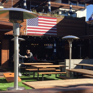 An american flag hangs above a patio area with tables and heaters