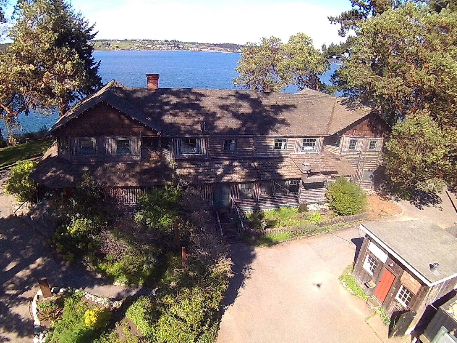 Lakeside cabin with trees and a gravel driveway, viewed from above in bright sunlight