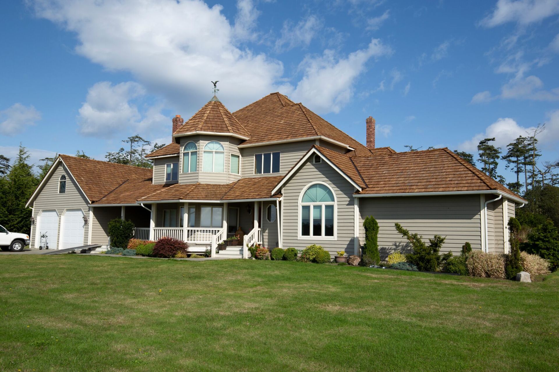 Large beige suburban house with a red-tiled roof and manicured green lawn under a blue sky
