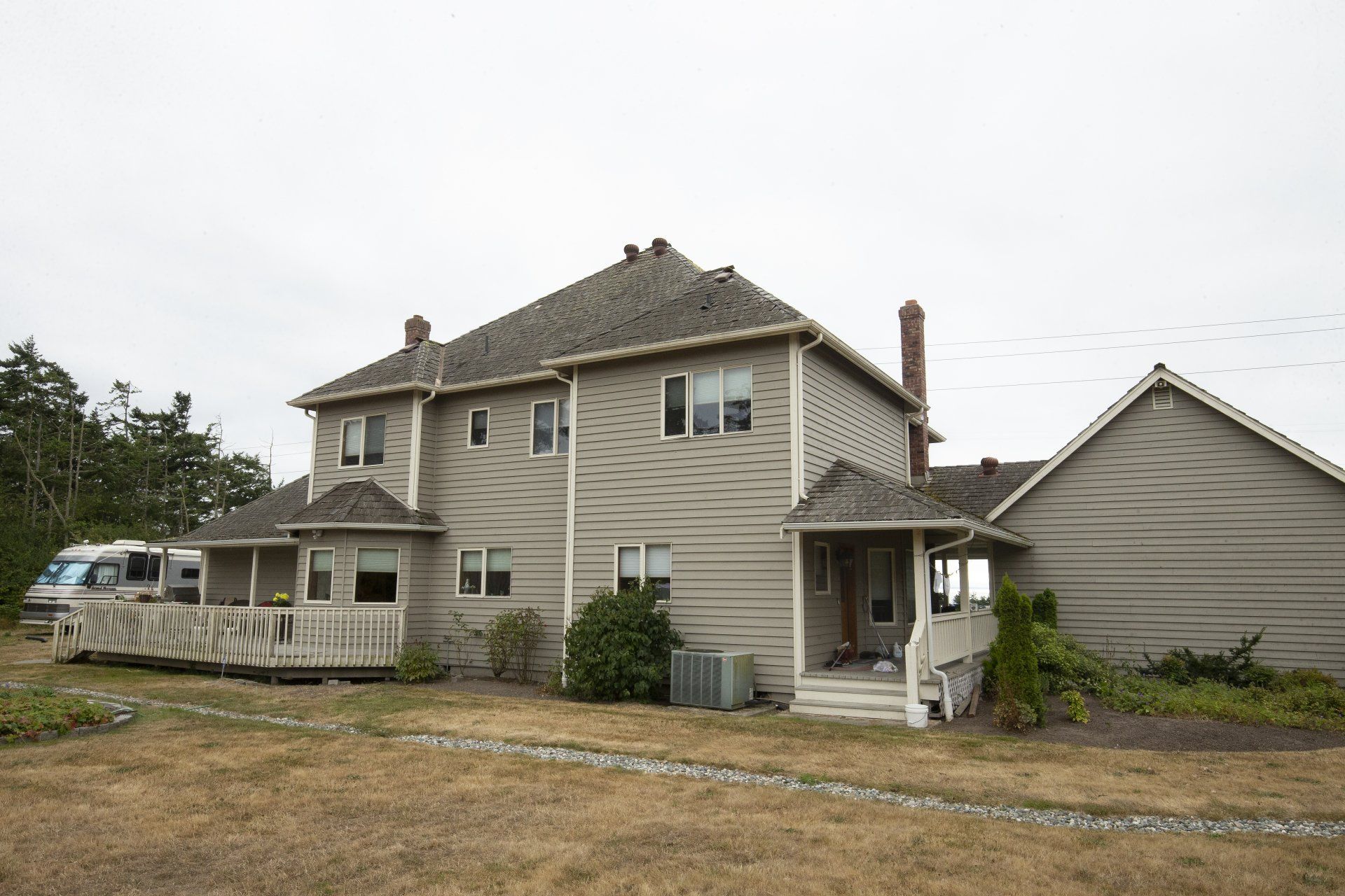 Two-story beige house with a porch and detached garage on a gravel lot under an overcast sky