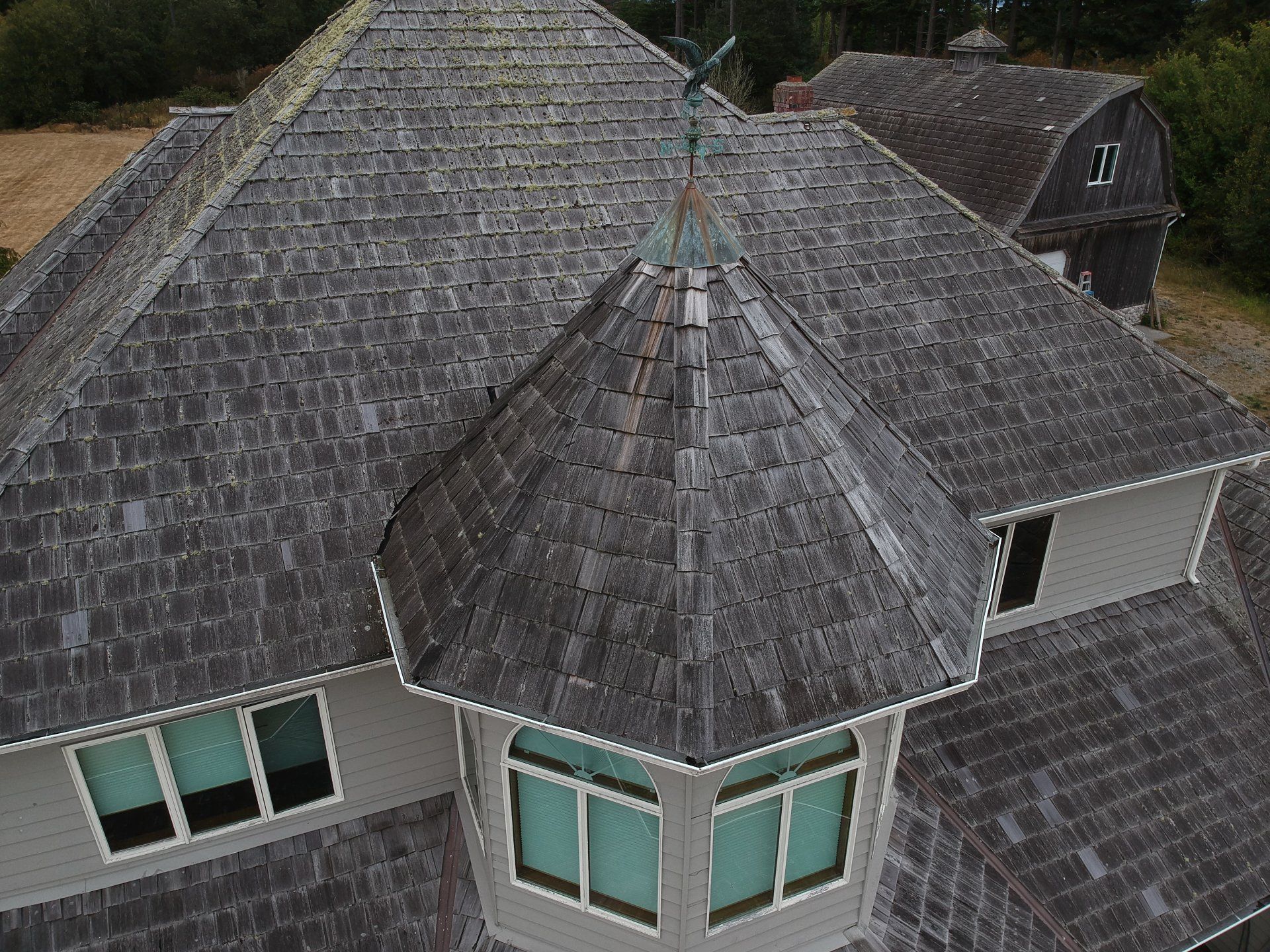 Aerial view of a dark gray shingled house roof with multiple gables and turquoise windows below.