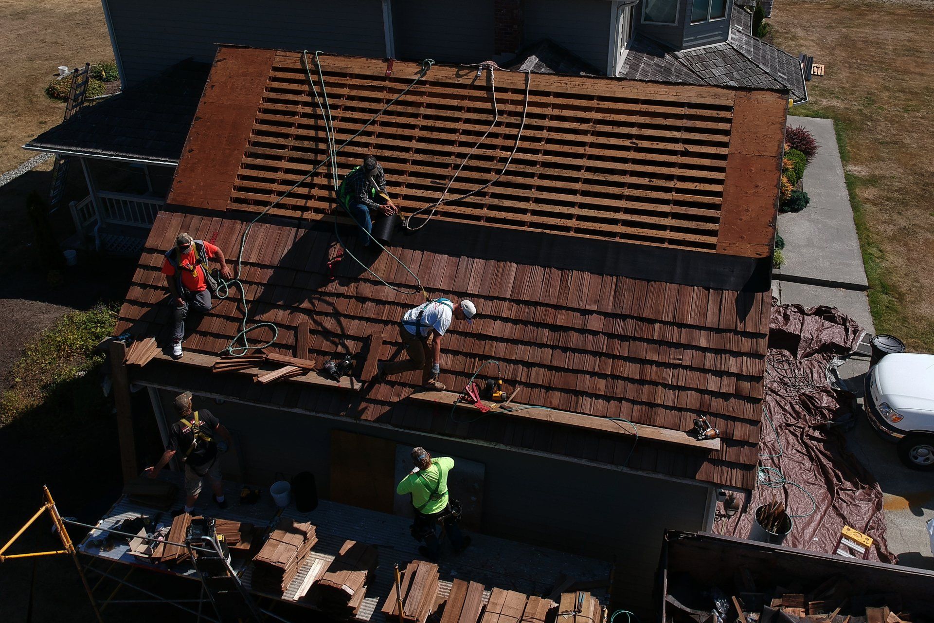 Workers repairing a red-tiled roof with tools and safety gear on a residential house