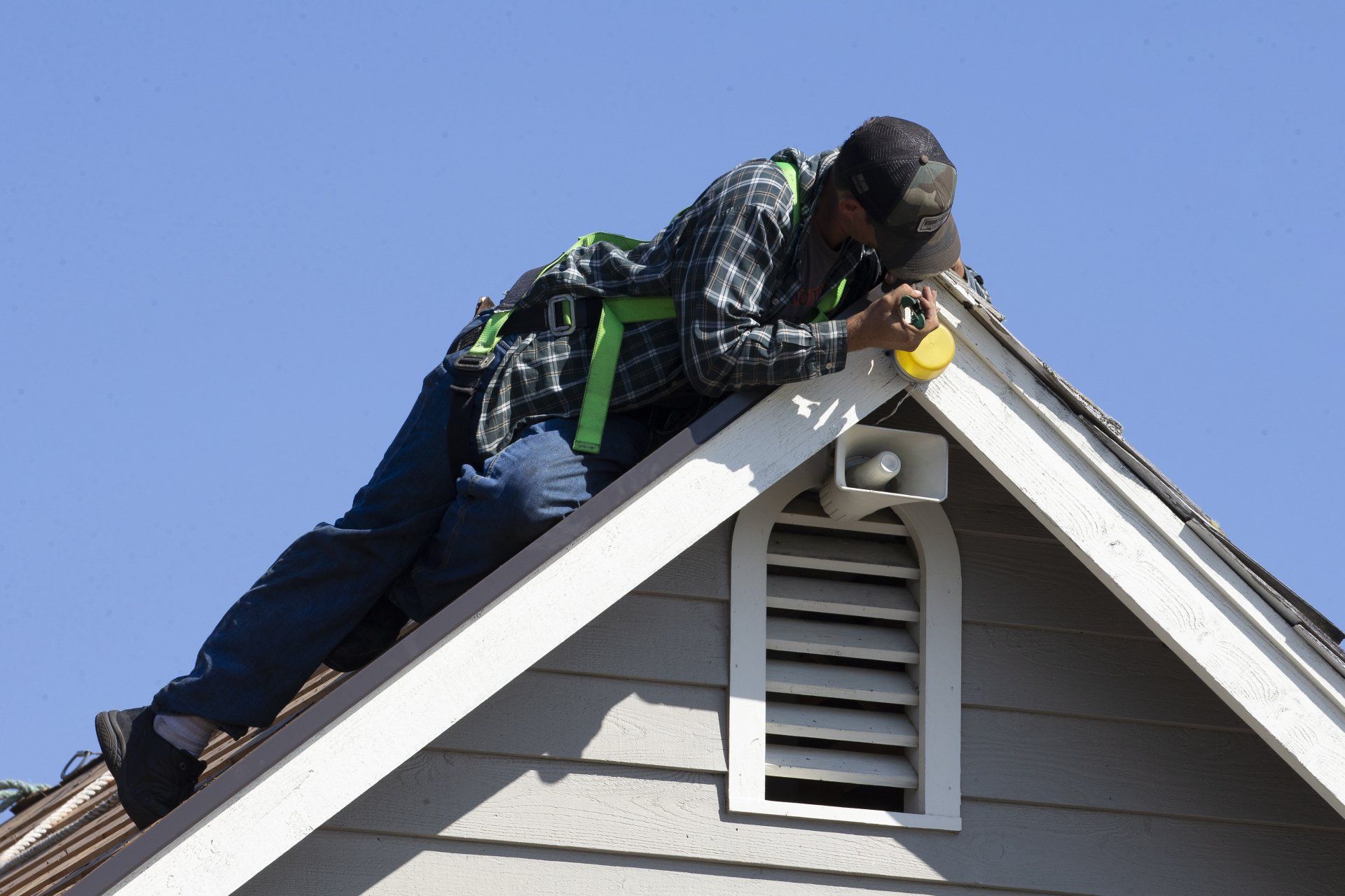 Worker on a roof using a saw near the ridge of a house under a clear blue sky