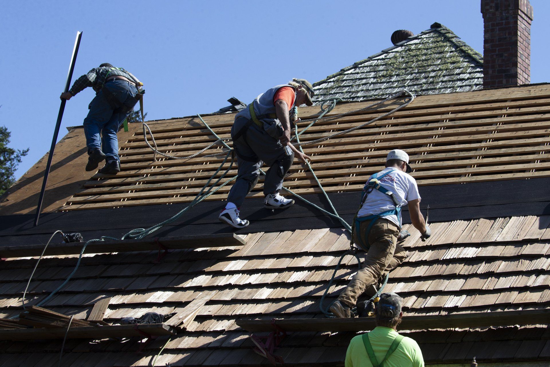 Workers repairing a roof, some replacing shingles on a house roof under a clear sky.