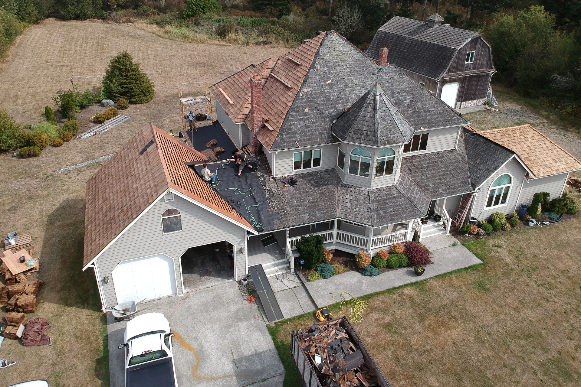 Aerial view of a large gray house with a red roof, driveway, and yard.
