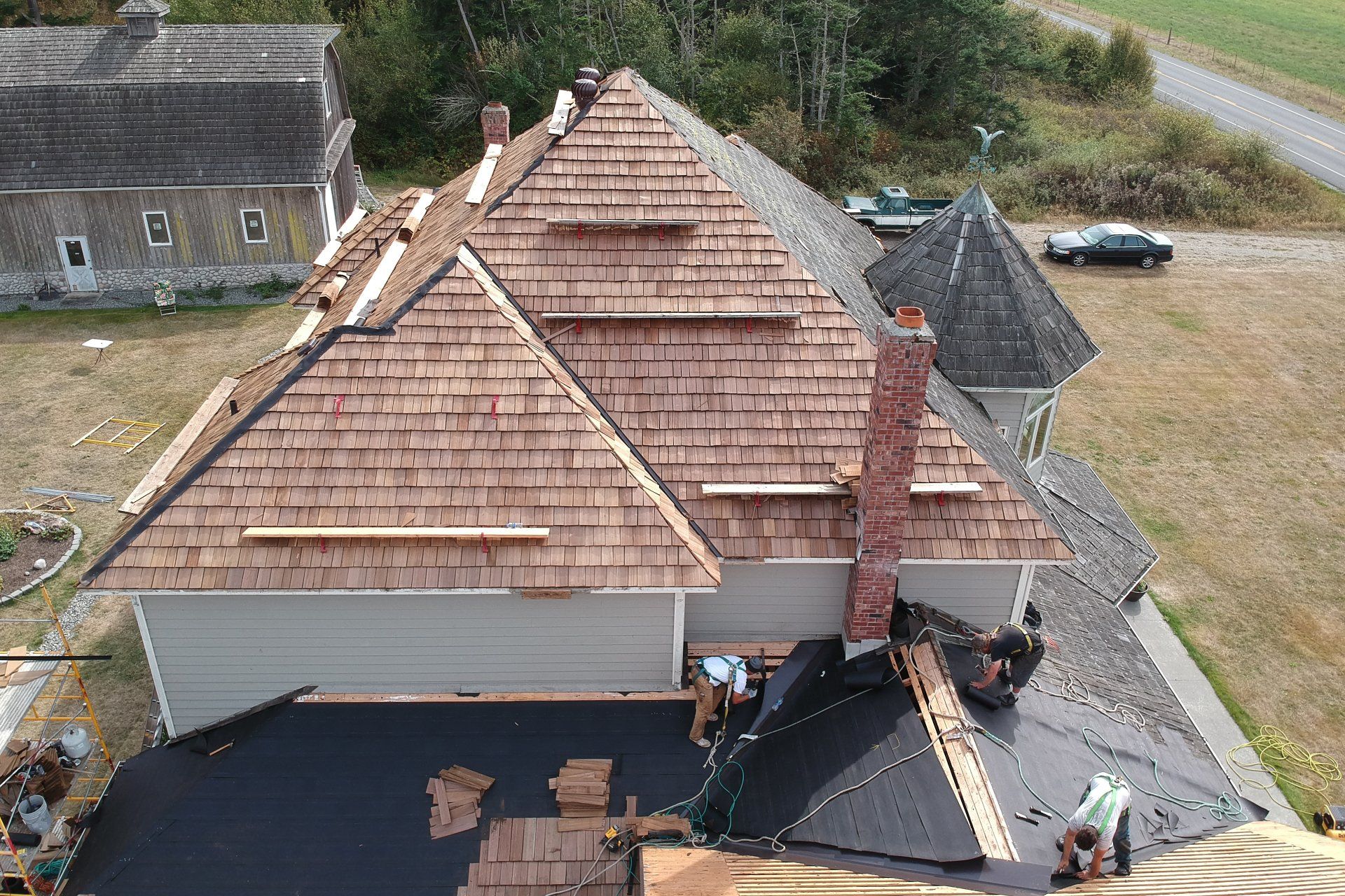 Aerial view of a house with a new brown shingle roof under construction, with workers below.