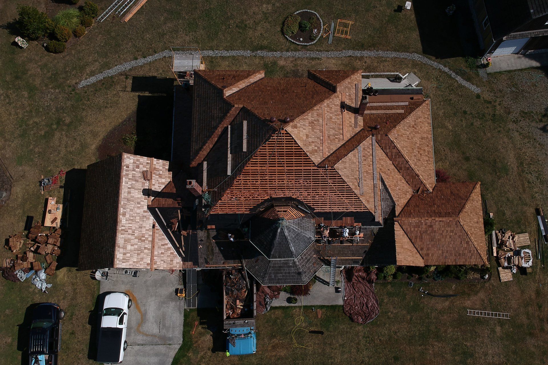 Aerial view of a house with a red-tiled roof, driveway, parked cars, and surrounding yard.
