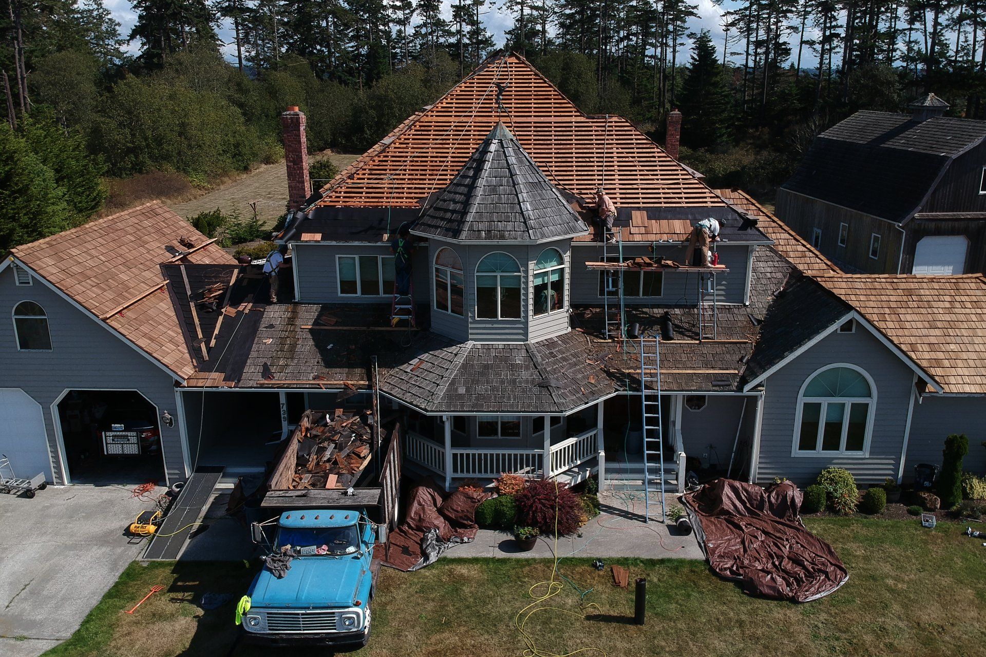 Aerial view of a house with a partially shingled roof, blue truck, and construction materials in the yard