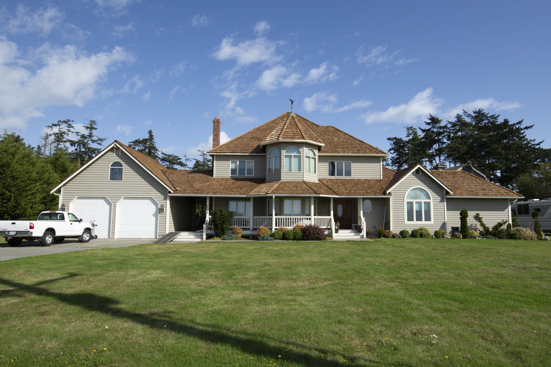 Large suburban house with a beige facade, white garage, and wide green lawn under a blue sky.