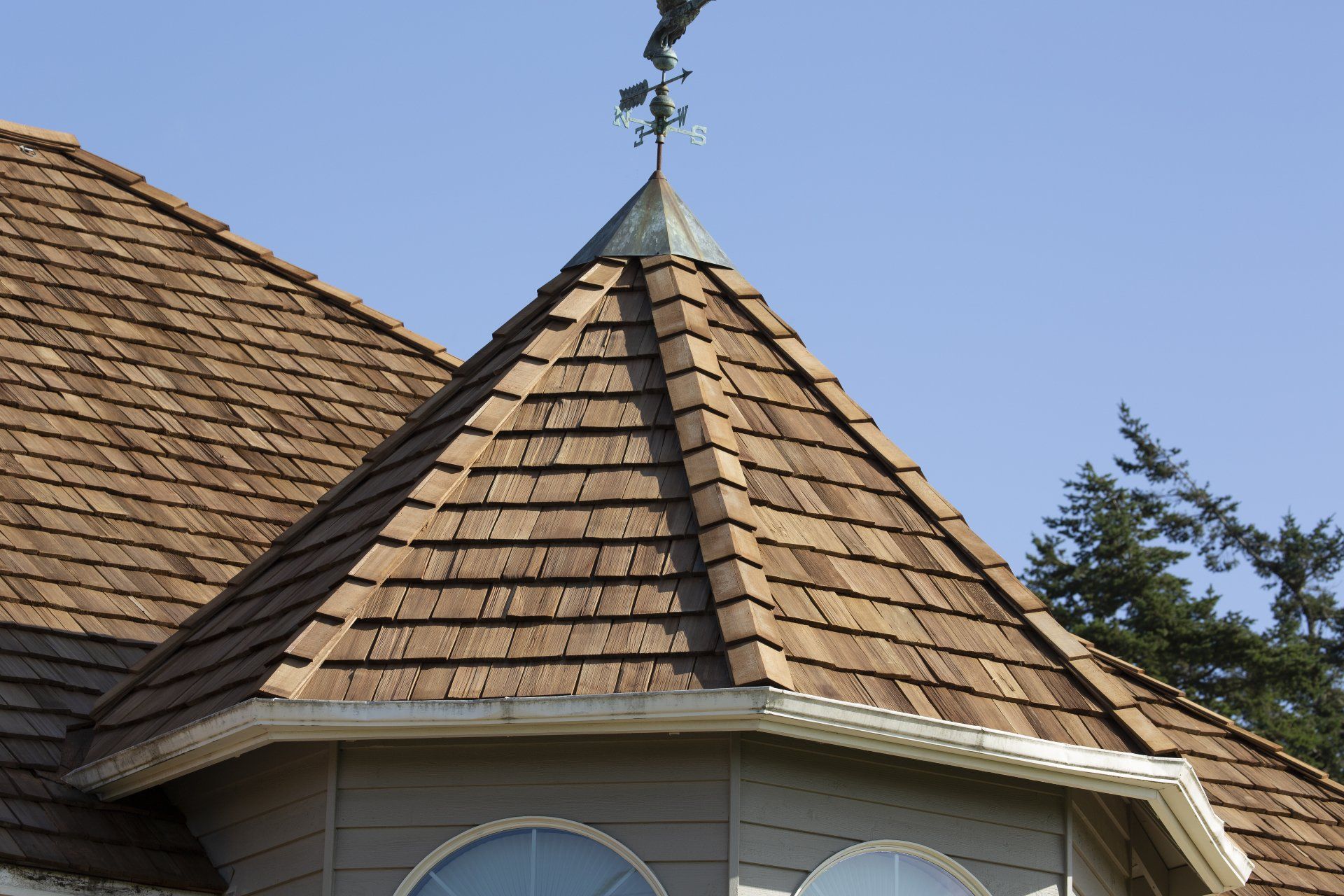 Shingled roof turret with weather vane against a blue sky